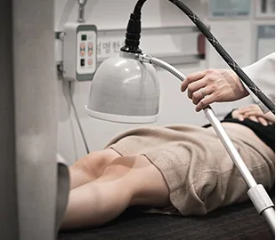 설명한의원 진료실에서 적외선 조사기를 다리에 비추며 휜다리 교정 관련 한방 물리치료를 진행하는 모습